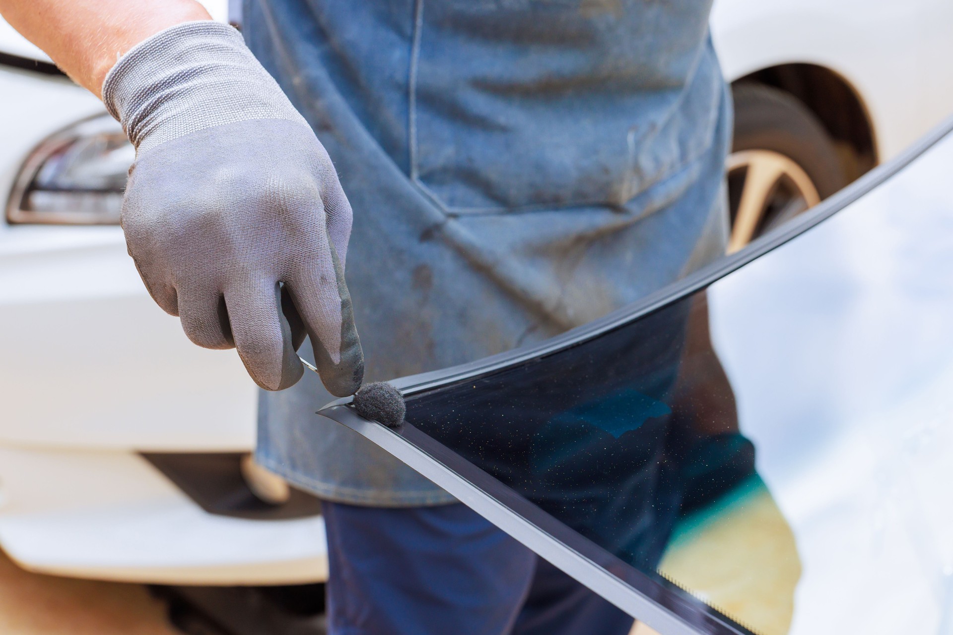 Professional technician installs adhesive for windshield replacement in auto service shop